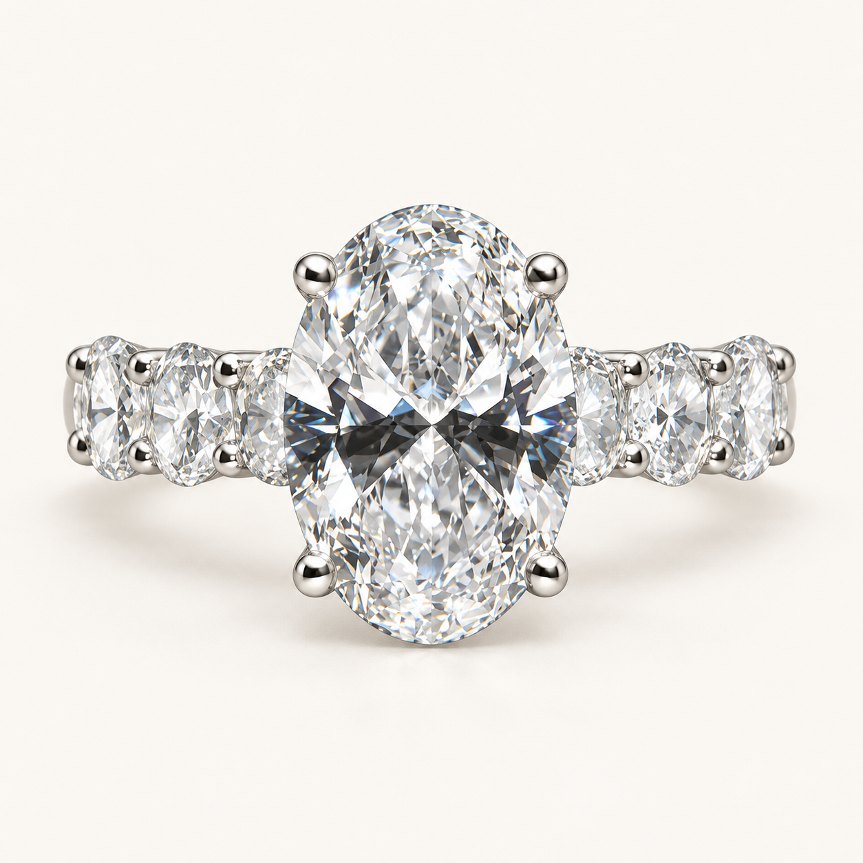 An elongated oval diamond with four prongs and oval side stones in a white metal setting
